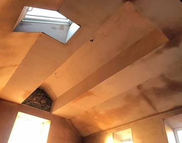 Freshly plastered loft ceiling with angled beams and skylight, showing smooth, even surfaces and clean edges that highlight expert plastering services.