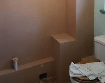 Freshly plastered bathroom wall with smooth brown finish and boxed-in pipework beside a white toilet, showcasing neat, precise plastering work and clean edges typical of professional interior finishing.