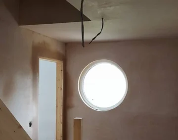 Freshly plastered interior wall with a circular window and doorway, showing smooth, even plasterwork and clean edges that highlight skilled craftsmanship during renovation.