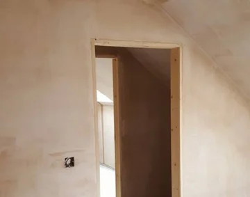 Freshly plastered interior wall and door frame in a loft space, showing smooth, even plasterwork and clean edges that highlight skilled plastering around a door frame.