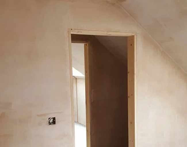 Freshly plastered interior wall and door frame in a loft space, showing smooth, even plasterwork and clean edges that highlight skilled plastering around a door frame.