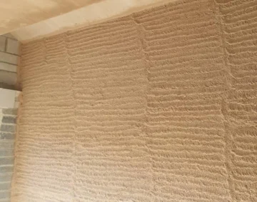 Close-up of a newly plastered interior wall with a textured scratch coat finish, showing horizontal grooves for improved adhesion before final plastering, highlighting skilled preparation work in construction.